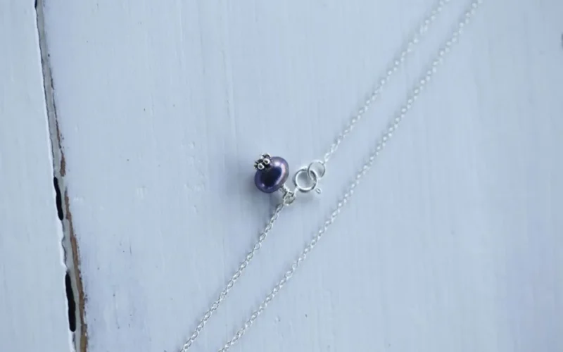Close-up of a silver necklace with a purple bead pendant on a wooden surface.