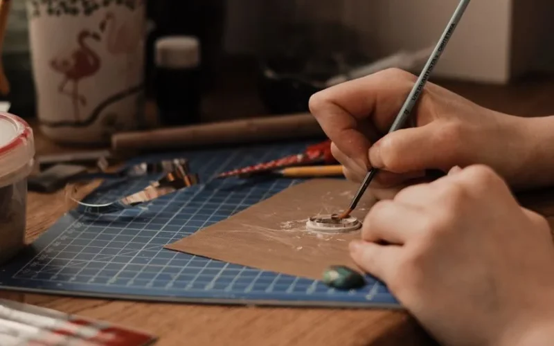 A close-up view of a person crafting jewelry using precision tools and clay indoors.