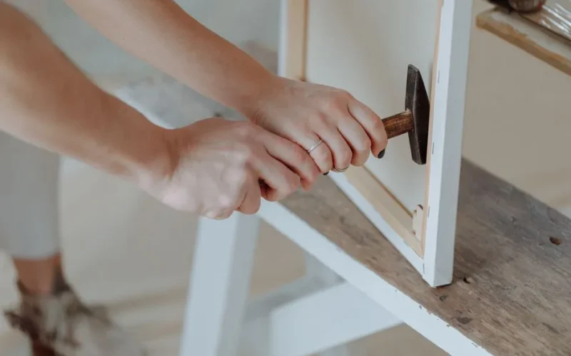 A detailed shot of hands using a hammer to assemble a wooden frame on a bench.