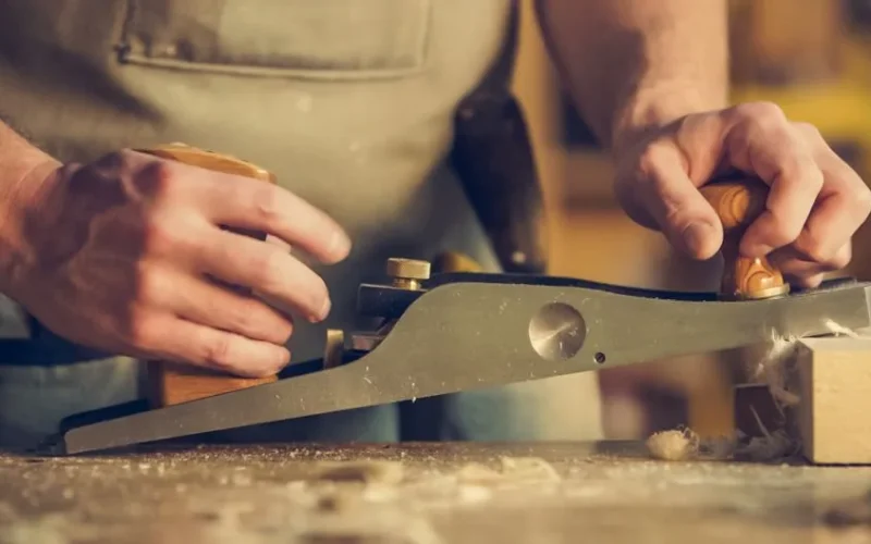 A carpenter skillfully using a hand plane on a wooden surface indoors.