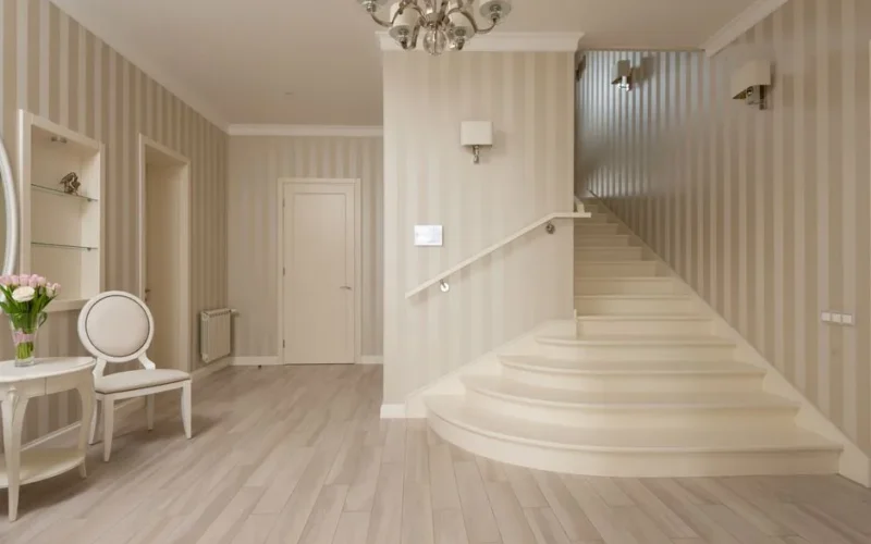 Interior of spacious cozy hallway with beige striped walls and light stairs and furniture