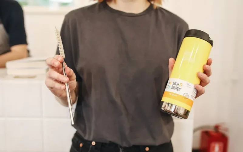 A woman holds a reusable thermos and metal straw, promoting zero waste lifestyle.