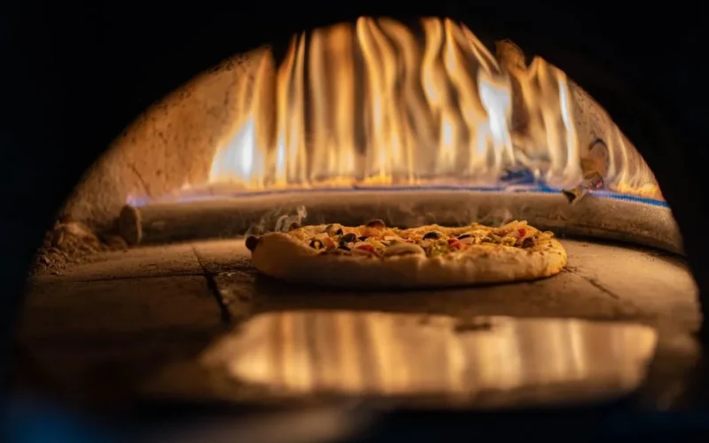 A delicious pizza baking in a traditional wood-fired oven with vibrant flames.
