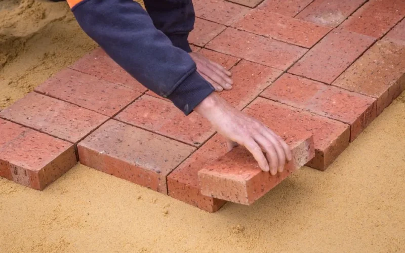 From above crop unrecognizable construction worker in uniform laying bricks on ground in daylight