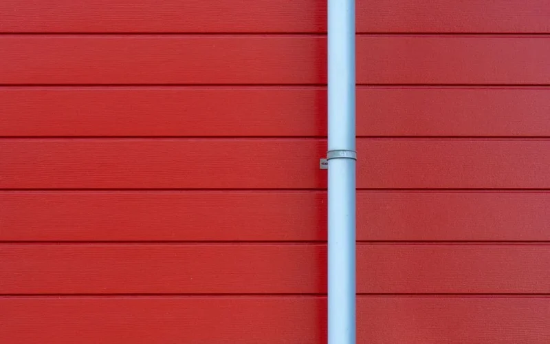 A minimalist photo of a red wall with a white rain gutter, showing clean lines and vibrant color contrast.