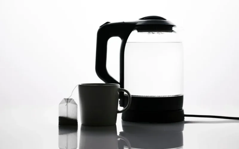 Minimalist image of a teabag beside a mug and electric kettle, emphasizing tea essentials.