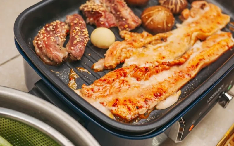 Delicious Korean BBQ with pork belly, beef, mushrooms, and garlic sizzling on an electric grill.