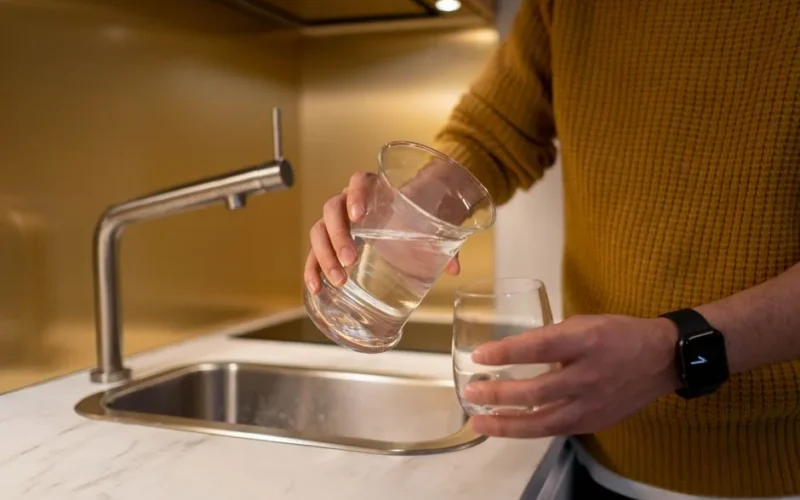 Person pouring water from a pitcher into a glass in a contemporary kitchen setting.