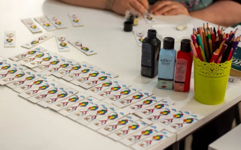 Close-up of crafting setup with playing cards, paints, and pencils on a table.