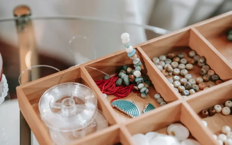 Wooden container with abundance of colorful beads and elastic cord for making bracelet placed on glass table in light room