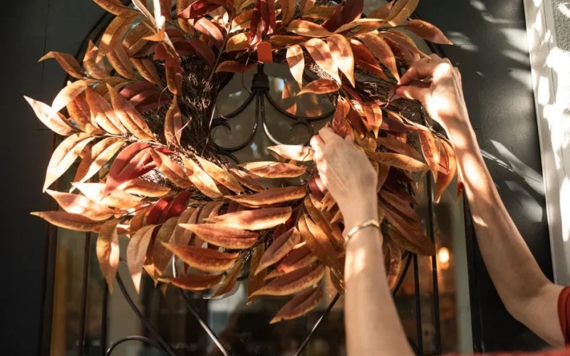 A person adjusting a decorative autumn wreath on a front door, capturing the fall atmosphere.
