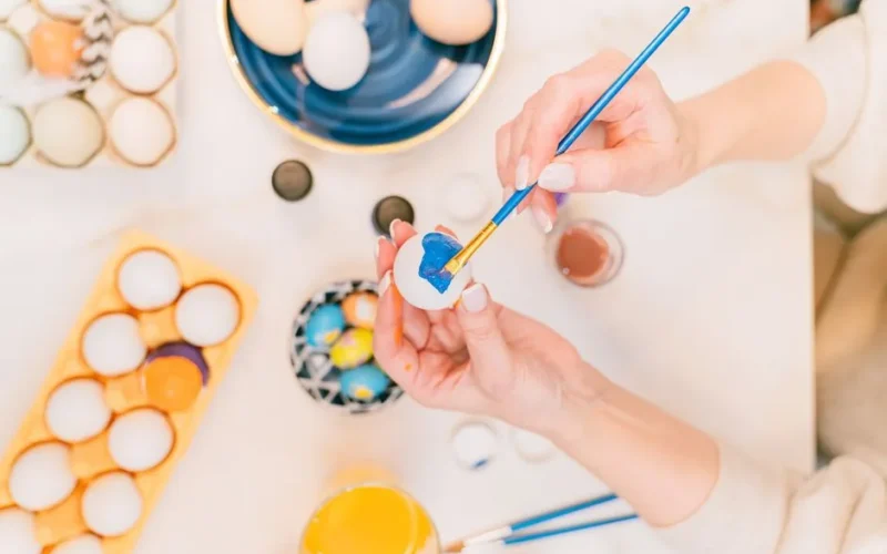 Person painting Easter eggs with bright colors indoors, showcasing creativity and holiday spirit.