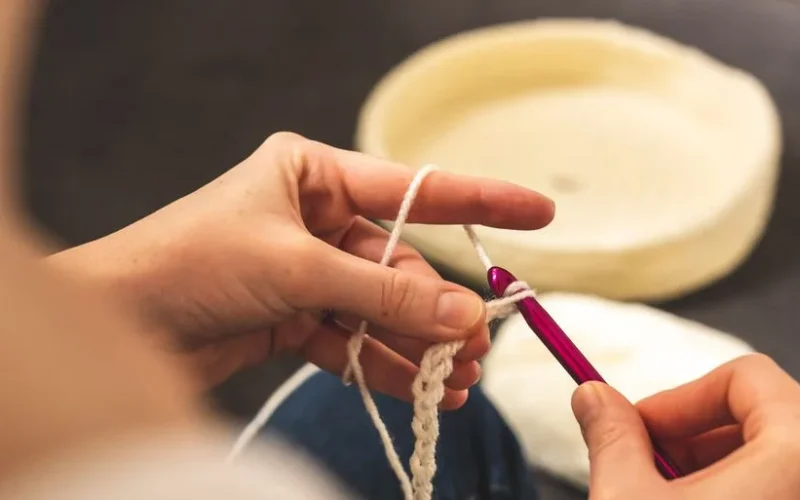 A focused shot of hands crocheting with a pink hook and white yarn, showcasing the art of crafting.