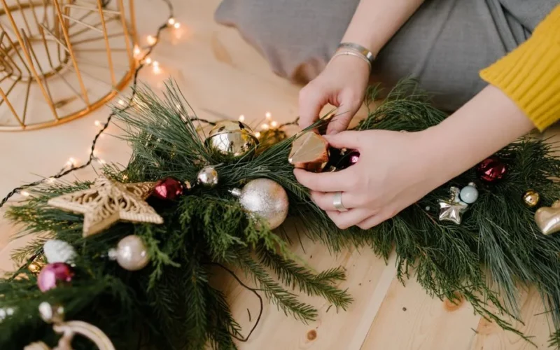 Close-up of hands decorating a Christmas wreath with ornaments, conveying holiday spirit.
