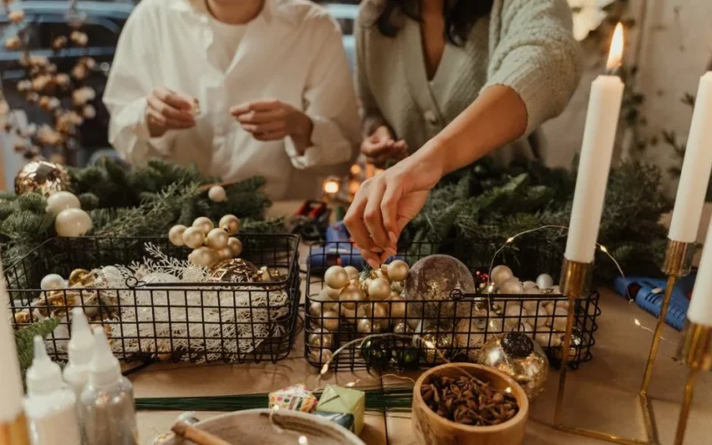 People crafting Christmas decorations with ornaments and candles indoors.