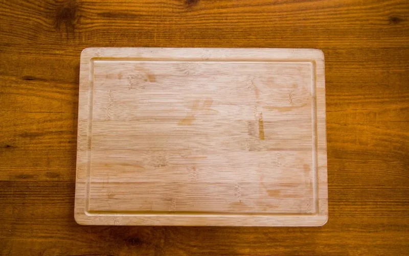 Top view of a natural wooden bamboo chopping board on a textured surface.