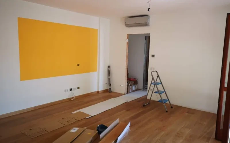A bright, empty room under renovation with ladder, tools, and wooden flooring.