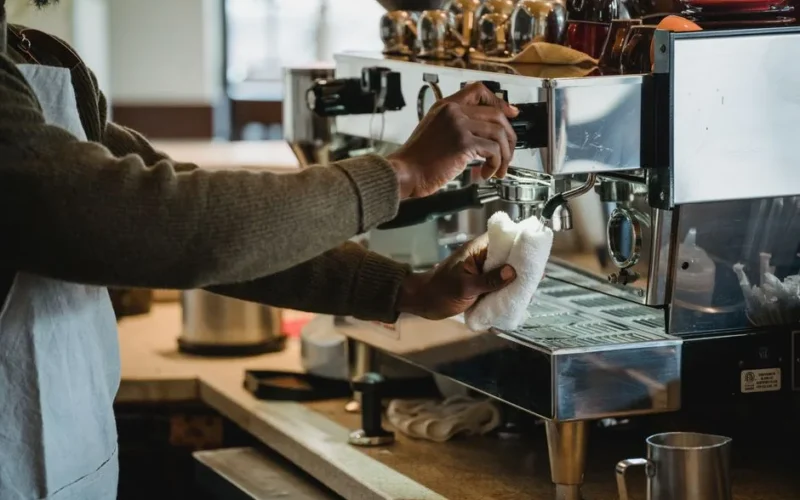A barista cleans the coffee machine at a café, ensuring hygiene and readiness for customers.