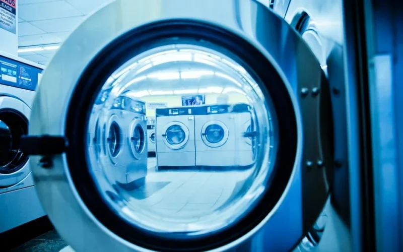 Interior view of a modern laundromat with rows of steel washing machines.