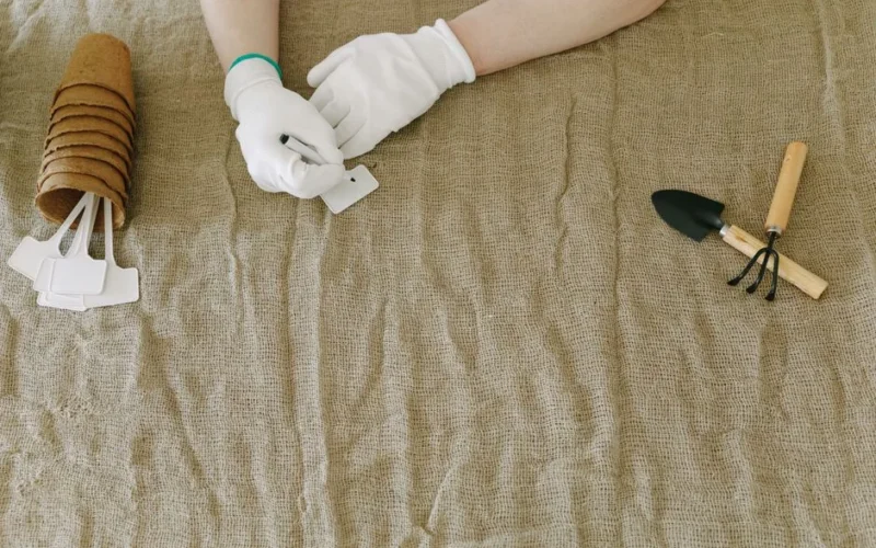 Person preparing gardening tools and labels on burlap surface, wearing gloves.
