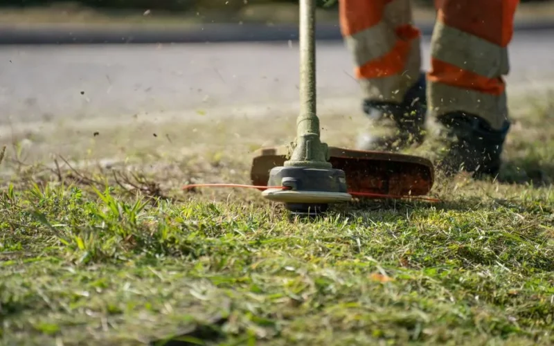 Close-up of a person trimming grass with a power tool outdoors.