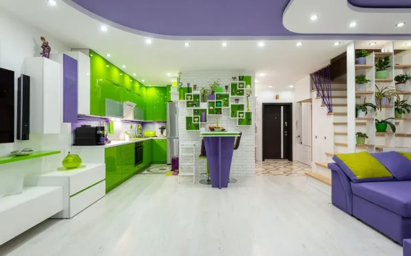 Creative interior of spacious studio apartment with bright green and purple furniture in living room and kitchen and modern appliances