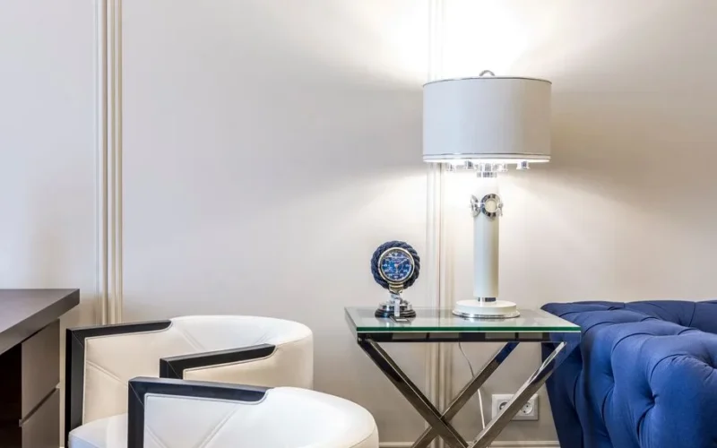 Interior of contemporary living room with small table and lamp near sofa and armchairs