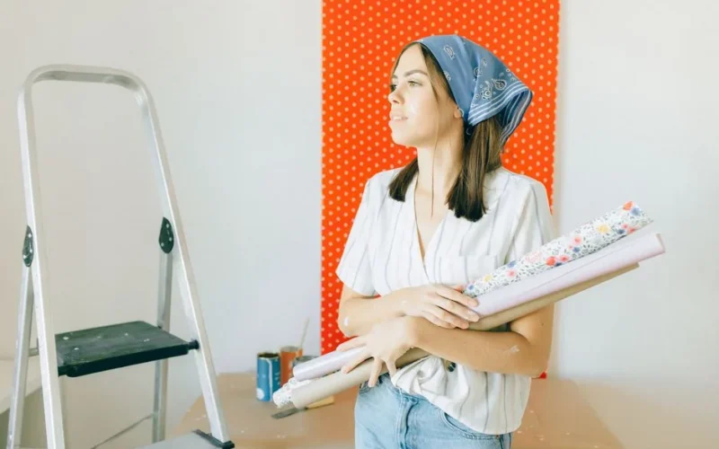 A young woman holding wallpaper is ready for room renovation indoors.