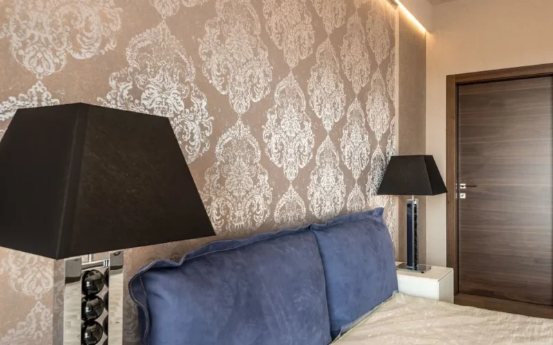 Modern bedroom with elegant wallpaper design, blue pillows, and stylish black lamps.
