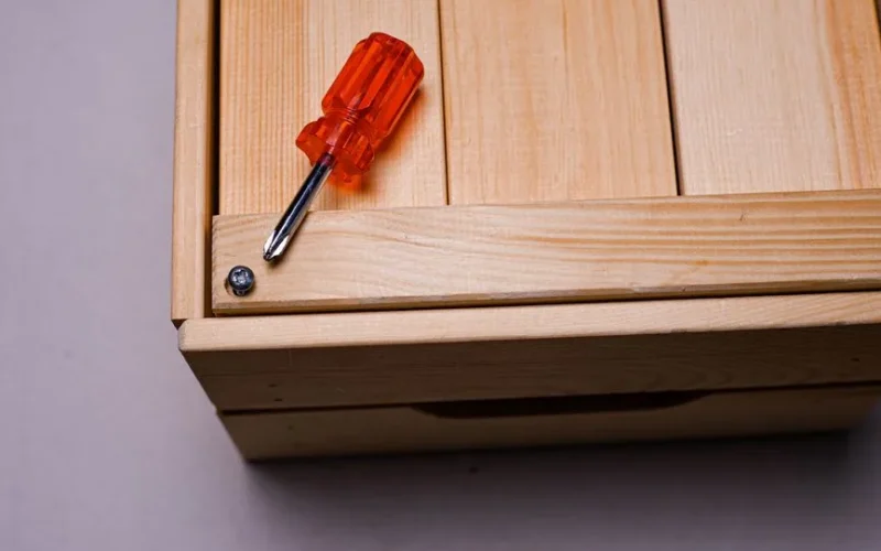 Minimalist image of an orange screwdriver beside a screw on a wooden box