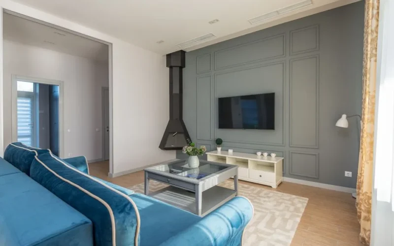 A stylish living room featuring a blue couch, wall-mounted TV, and elegant decor.