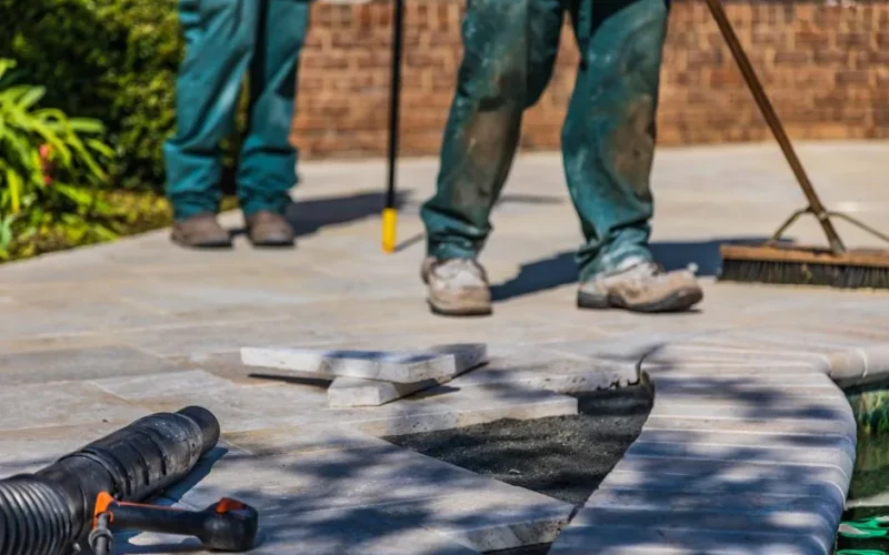 Workers laying tiles on an outdoor patio under sunlight.