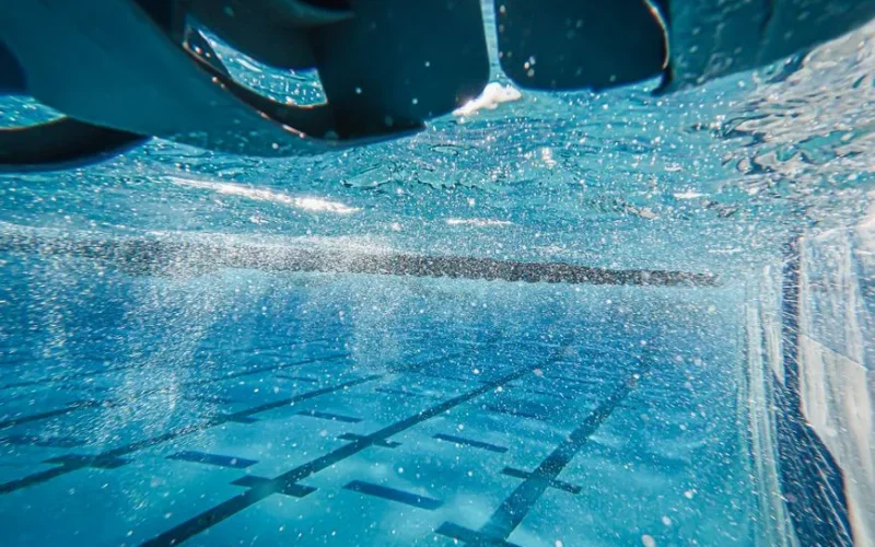 An underwater perspective capturing sparkling sunlight in a clear blue swimming pool.