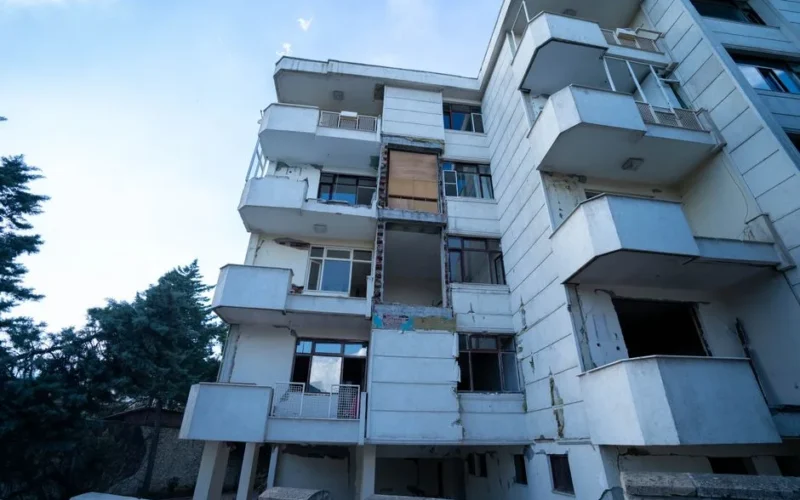 Low angle shot of a damaged residential building exterior with visible balconies and wear.