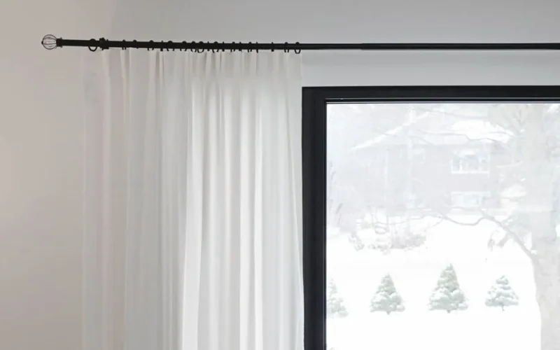 White curtains partially covering a window with a snowy outdoor view. Minimalist home decor.
