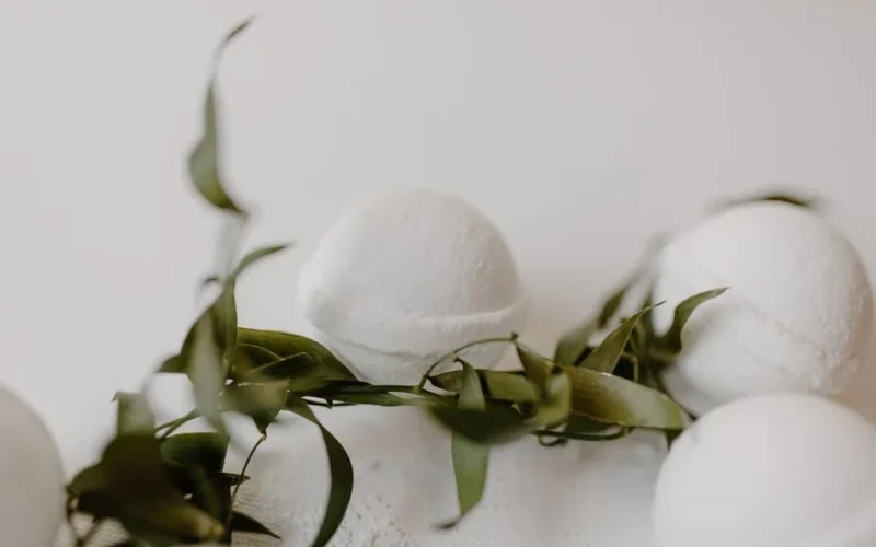 Minimalist bath bombs with eucalyptus leaves on a clean white surface for a serene bath experience.