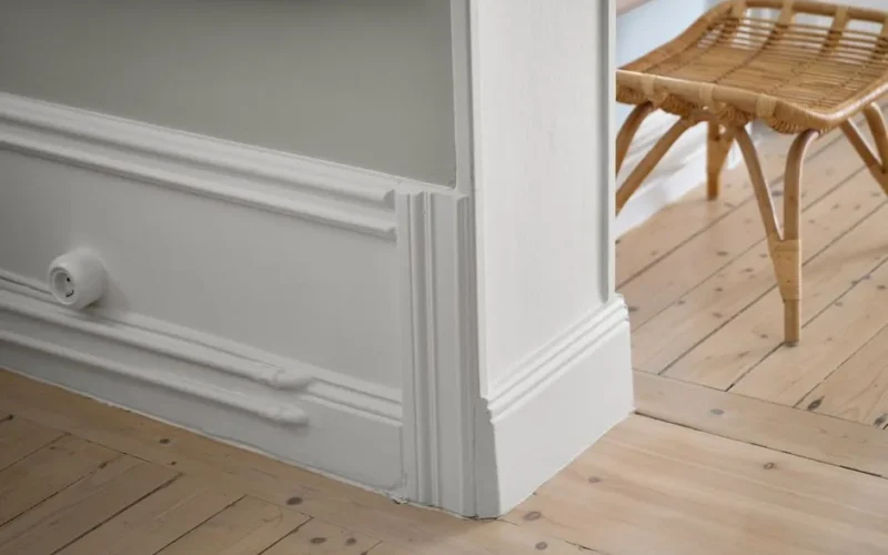 Stylish minimalist interior featuring a wooden floor, wicker chair, and elegant molding.