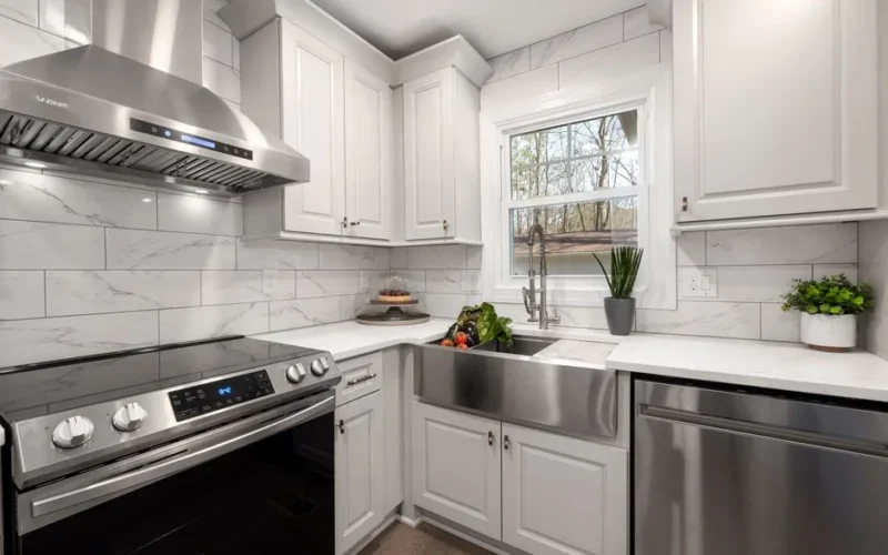 Stylish white kitchen featuring a stainless steel oven, sink, and range hood. Bright and contemporary design.