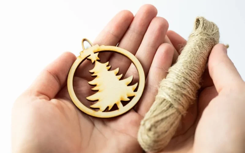 Wooden Christmas tree ornament held in hands with twine on a white background.