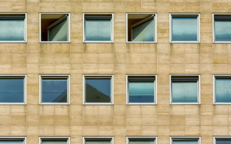 Detailed view of a modern office building facade featuring uniform sandstone tiles and windows with blinds.