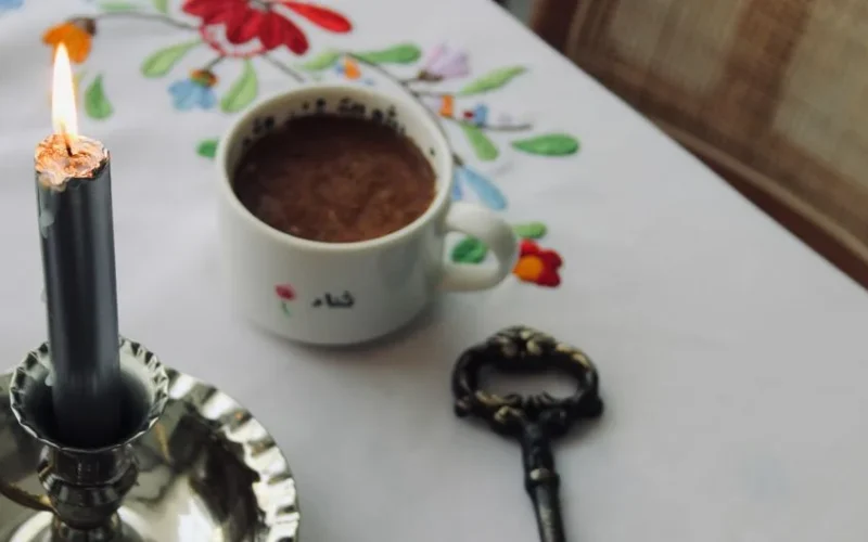 Warm and inviting setup with a cup of coffee, candlelight, and a vintage key on an embroidered tablecloth.