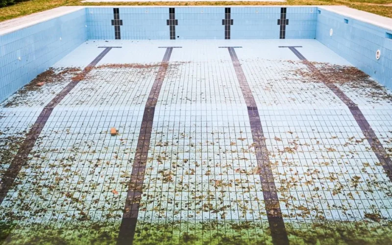 High angle view of an empty, abandoned swimming pool with leaves scattered on the tiled surface.