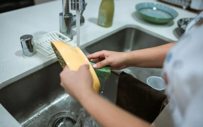 Close-up of hands washing dishes in a kitchen sink with running water.