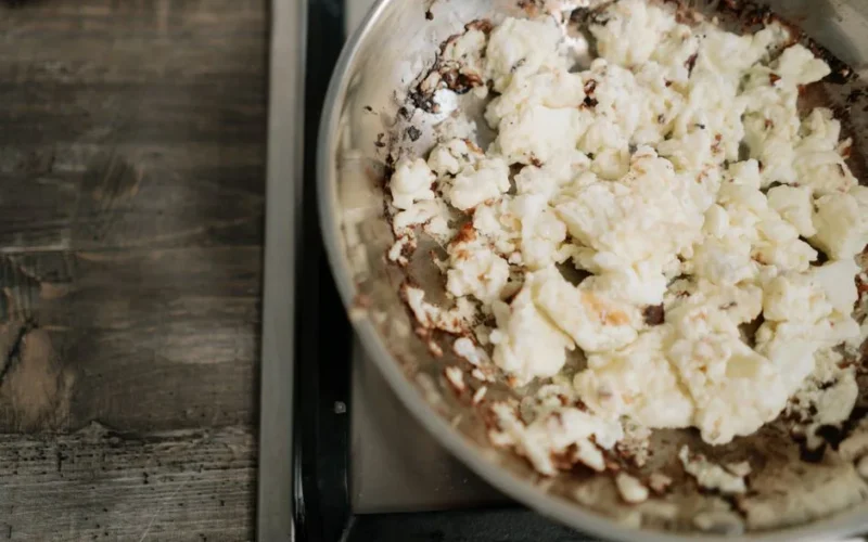 Overcooked scrambled eggs in a stainless steel skillet on a stove.