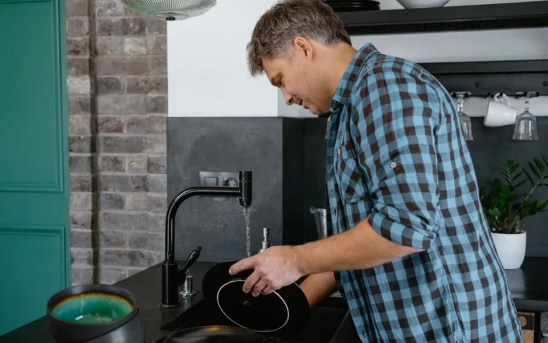 Middle-aged man in plaid shirt washing dishes in a contemporary kitchen.