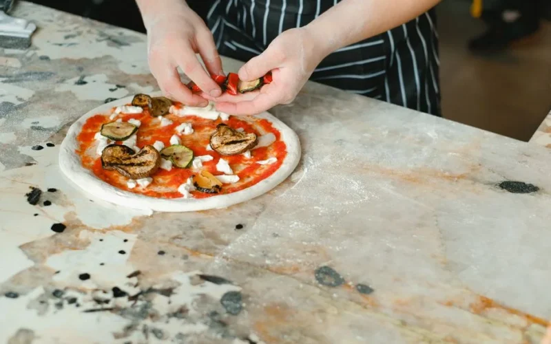 Close-up of a chef preparing a delicious vegetable pizza in a restaurant kitchen.