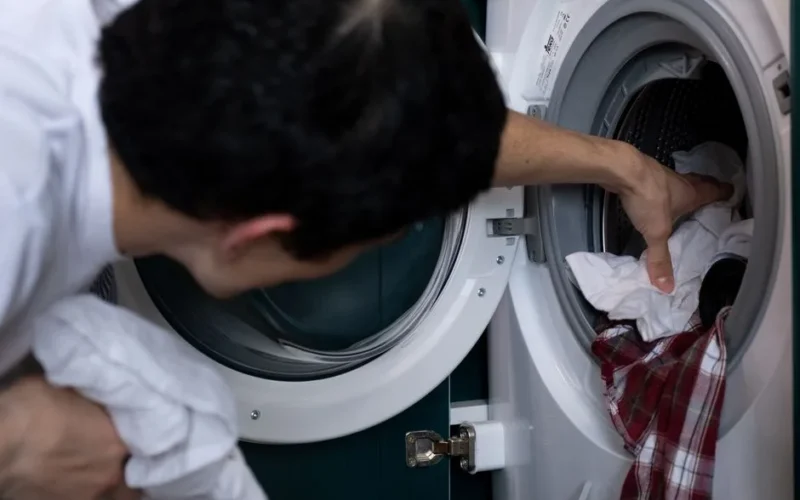 Close-up of a man placing clothes into a washing machine during household chores.
