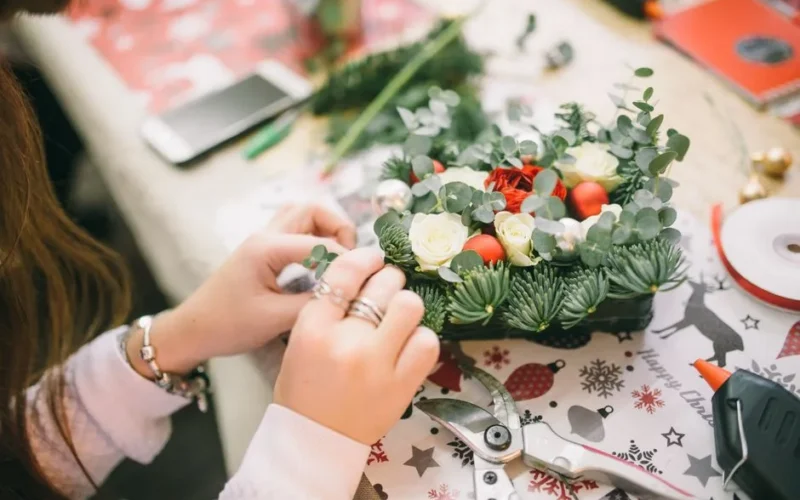 Hands crafting a Christmas floral arrangement with festive decorations.