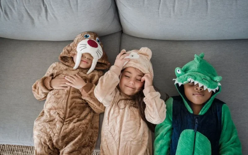 Three children in animal onesies relaxing on a couch, enjoying playful moments indoors.