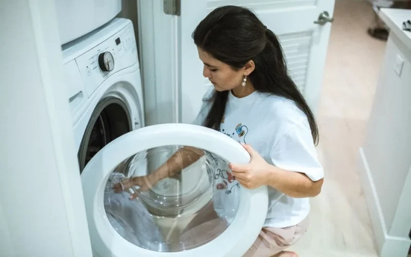 A woman kneeling to load clothes into a front-loading washing machine in a modern home laundry room.